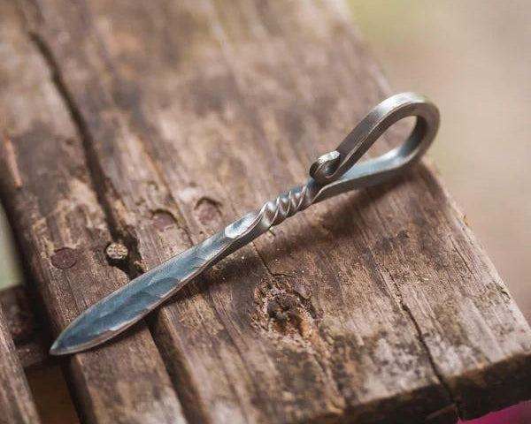Hand forged shellfish knife with twisted handle on rustic wood surface.
