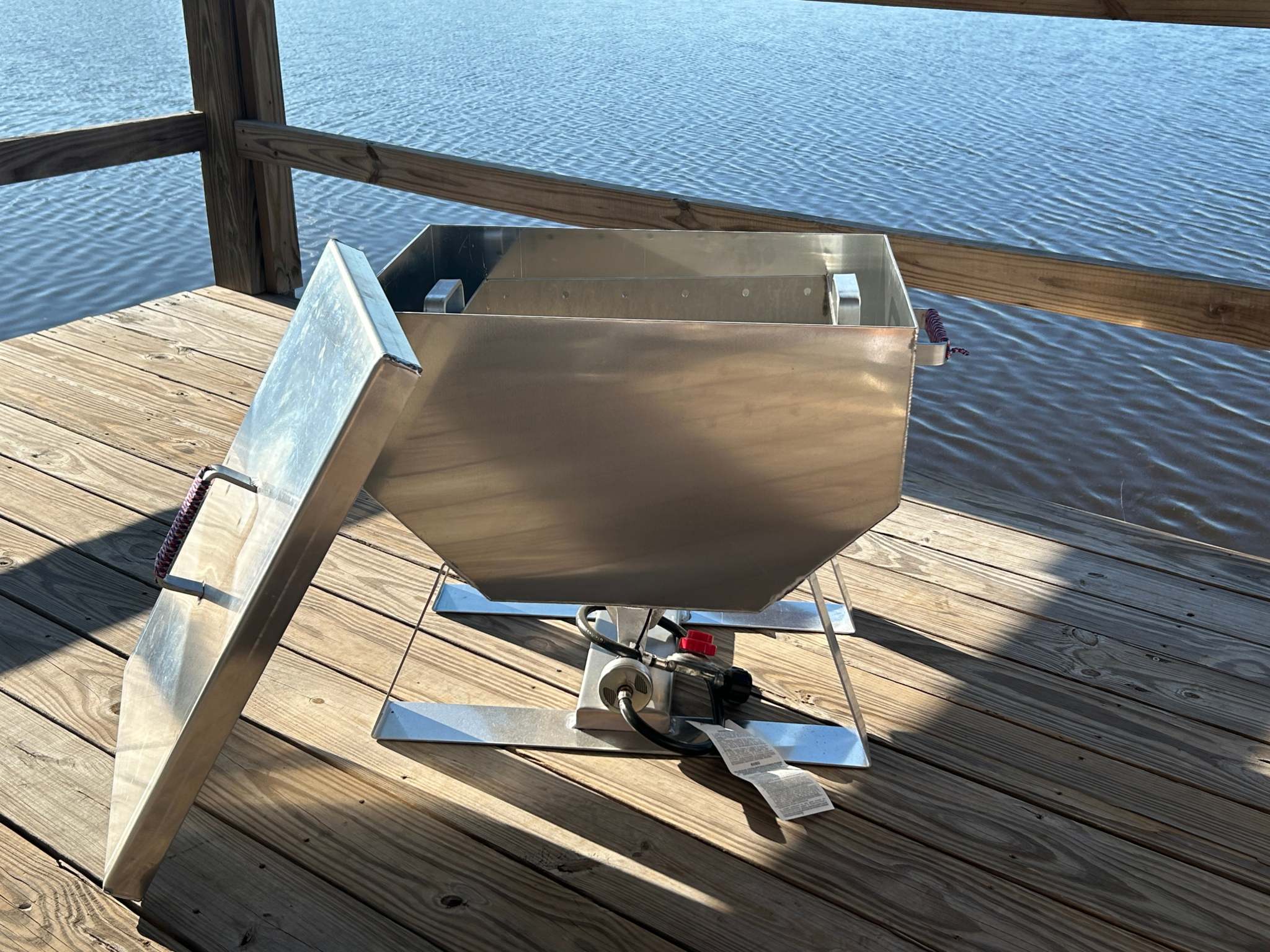 Rugged aluminum oyster steamer cooker on wooden deck by water.