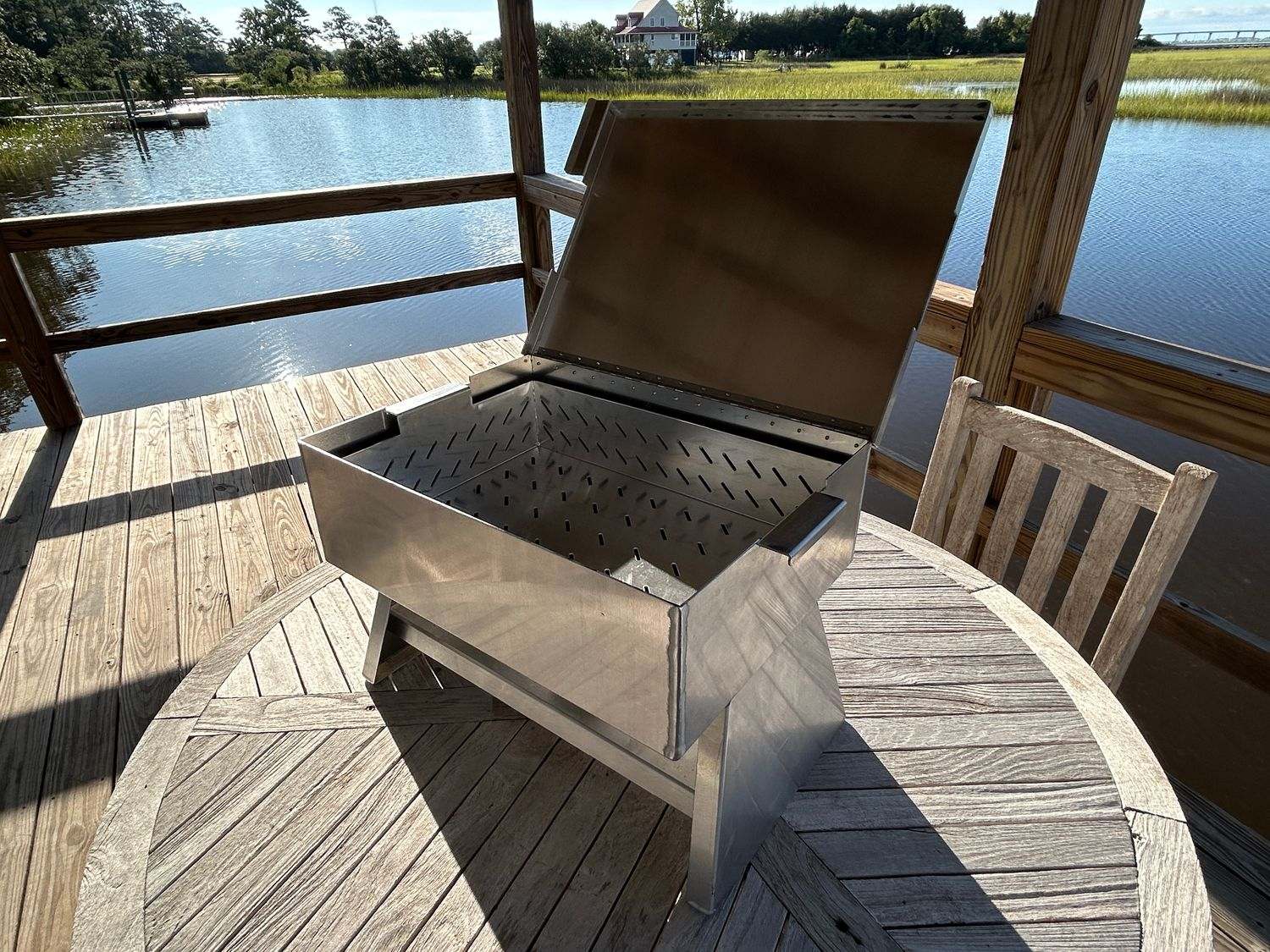 The Chuck 27-quart aluminum outdoor cooker on a wooden table by a lake.