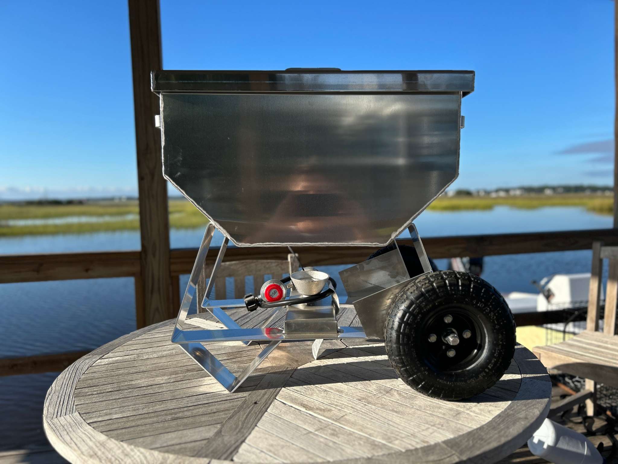 Wheeled Classic aluminum cooker on wooden table by waterside, featuring pneumatic tires for easy transport.