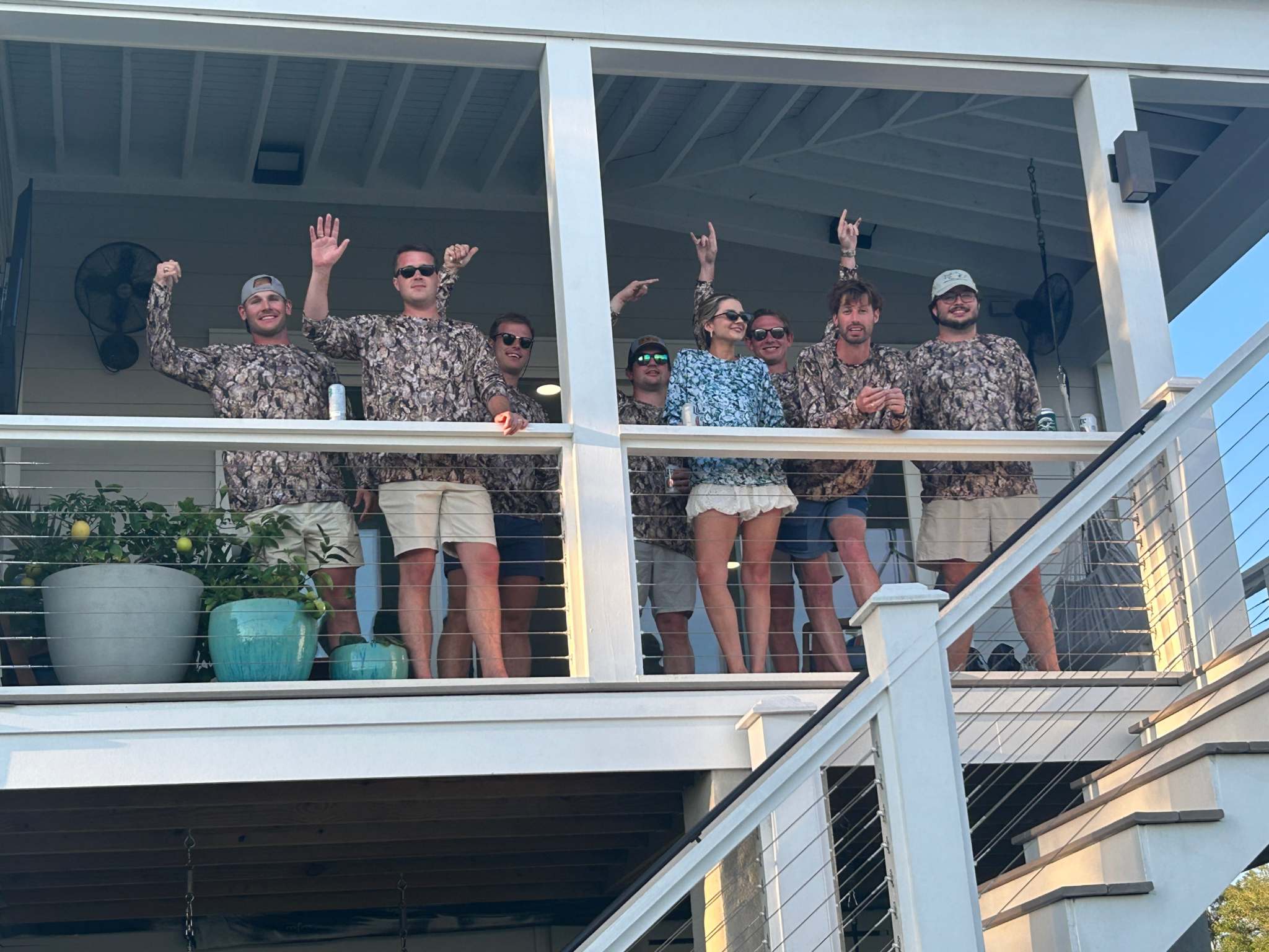 Group of people wearing Oystaflage Blue Point long sleeve performance shirts on a porch railing outdoors