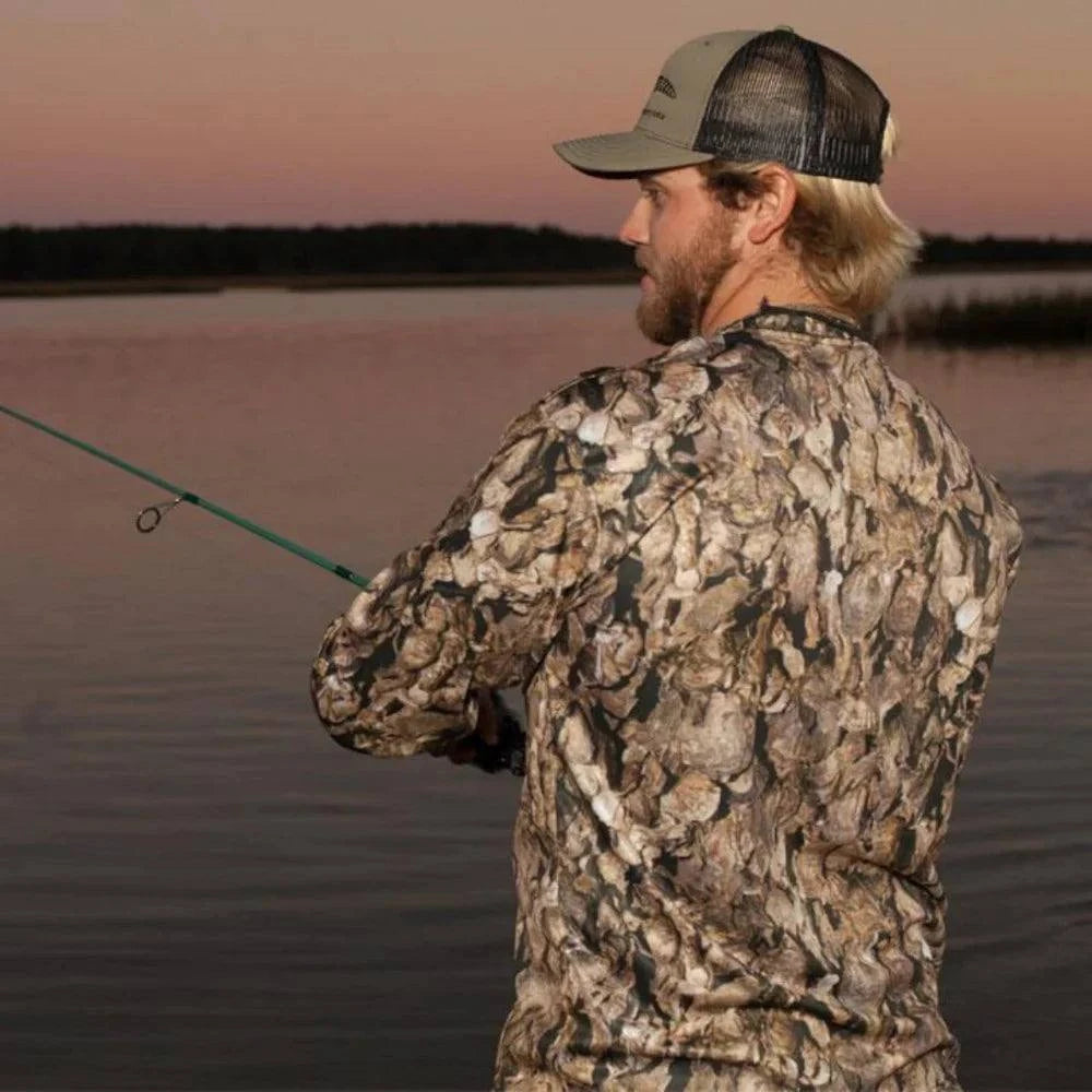 Man fishing wearing Oystaflage long sleeve performance shirt with oyster shell camouflage pattern at sunset by the water